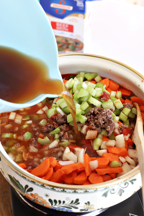 Adding beef broth to the pot for hamburger barley vegetable soup.