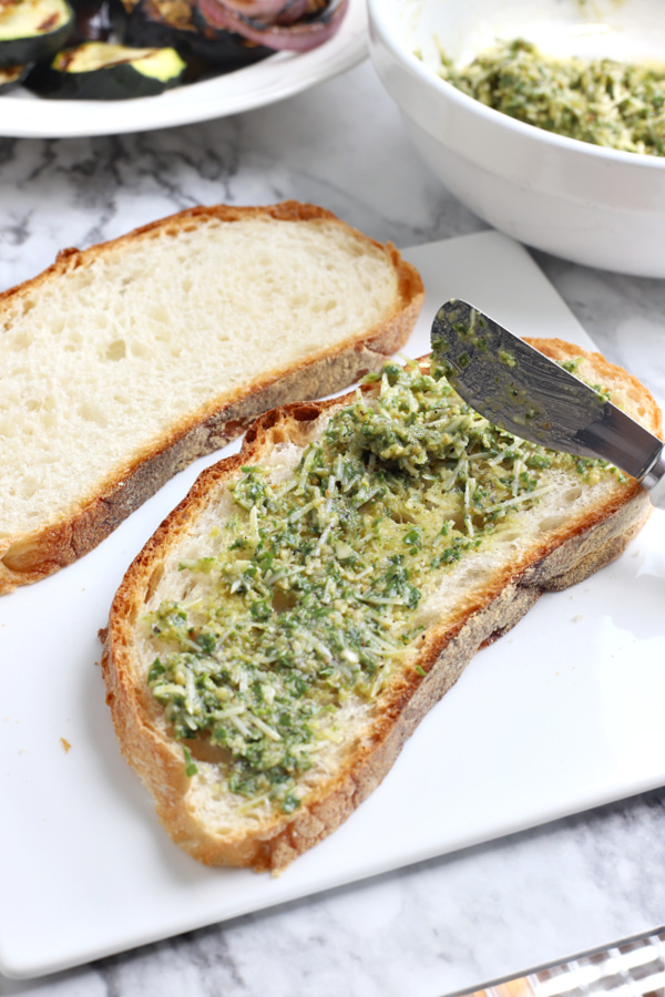 spreading fresh pesto basil on bread for grilled vegetable panini