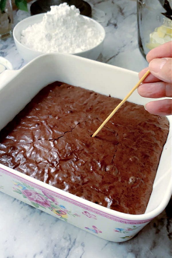 Testing brownies for doneness by inserting a toothpick for Peanut Butter Frosted Brownies.