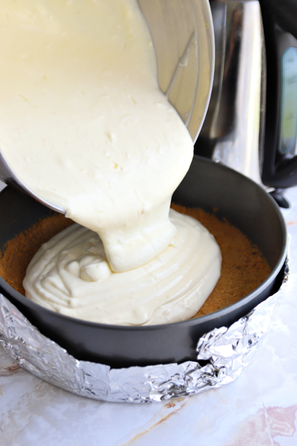 adding the cream cheese batter to the prepared springform pan for lemon curd cheesecake.