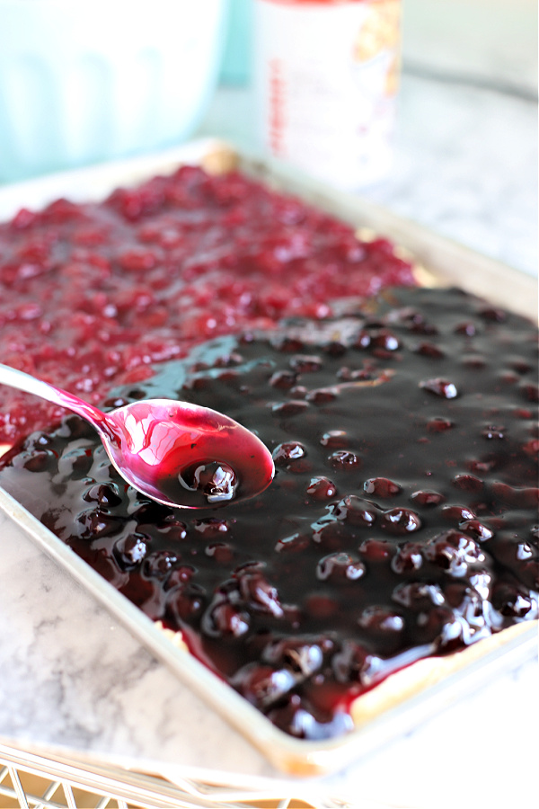 Spooning the cherry and blueberry pie filling onto the batter for fruit bars.