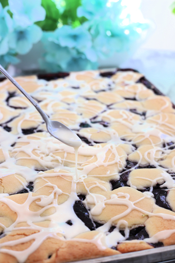 Drizzling frosting glaze onto cherry blueberry fruit bars.