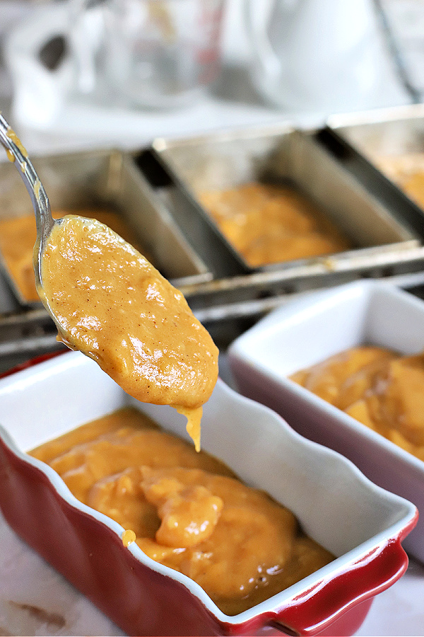 spooning pumpkin bread batter into prepared baking pans