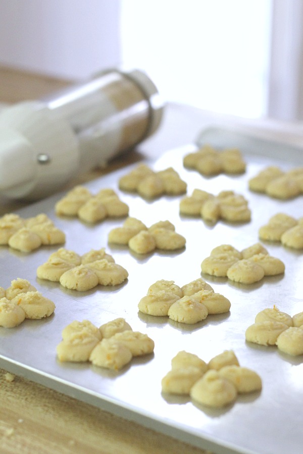 Frosted orange crisps are cookies flavored with orange in the dough and topped with a light orange frosting. They are crisp, tender and the citrus provides a nice surprise in each bite. Made using a cookie press similar to spritz or shortbread cookies but are sweeter. Perfect with a cup of tea, coffee or glass of milk.