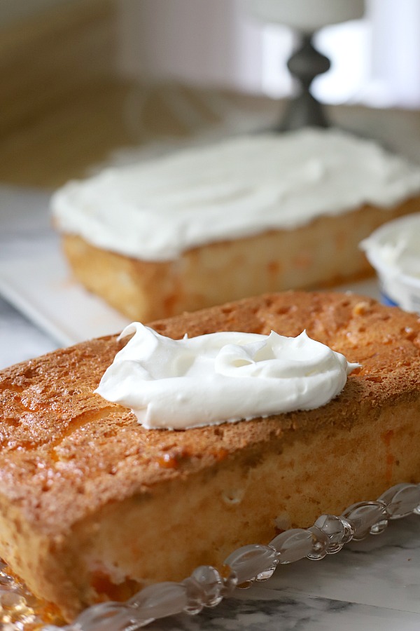 A light dessert and easy recipe for orange angel food cake begins with a box mix. Poke holes throughout the baked cake and pour in Jell-O. Top with whipped topping and serve.