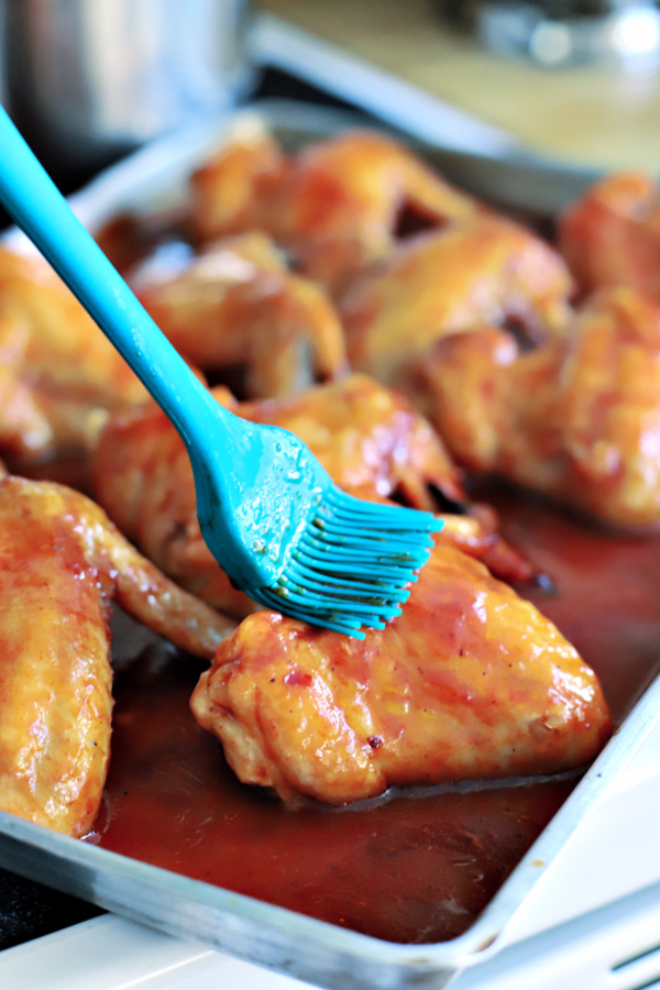 Basting sticky chicken wings with orange glaze