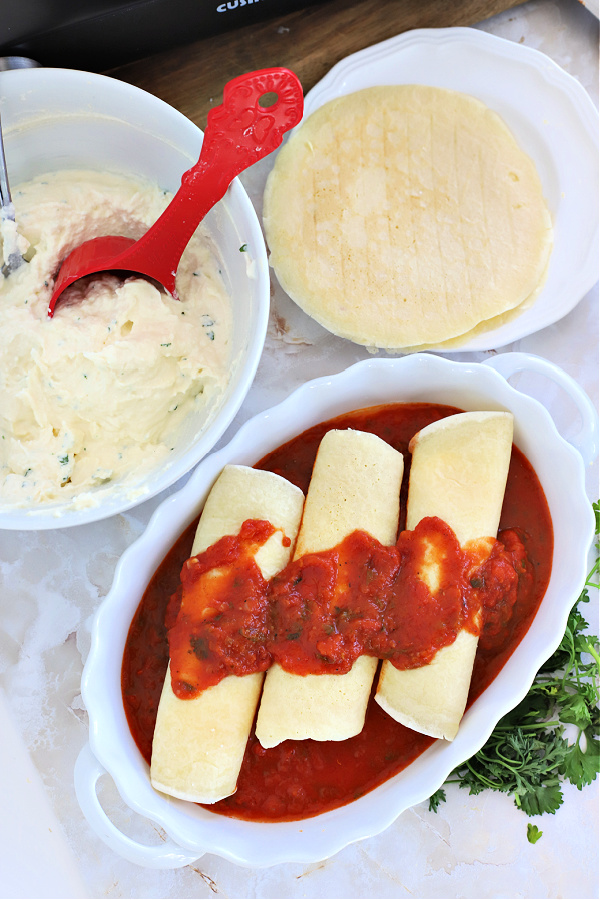 Adding tomato sauce over homemade manicotti crepes.