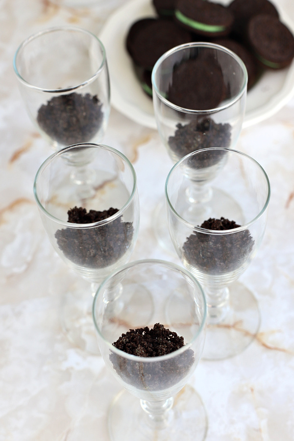 Layering the Oreo crumbs in glasses for the minty chocolate cheesecake no bake parfait dessert.