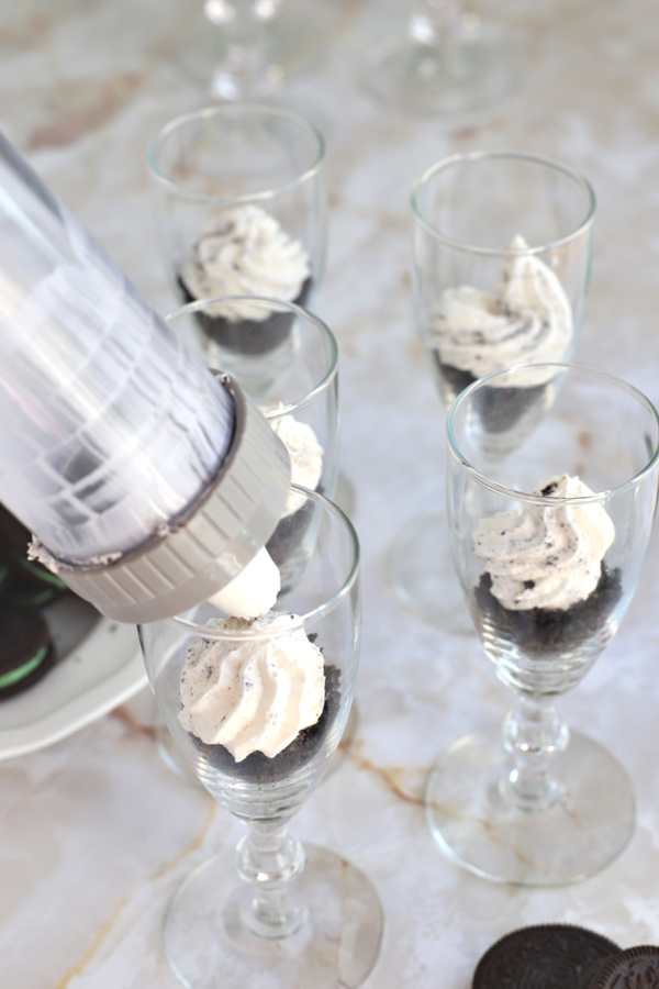 Layering the Oreo crumbs in glasses for the minty chocolate cheesecake no bake parfait dessert.