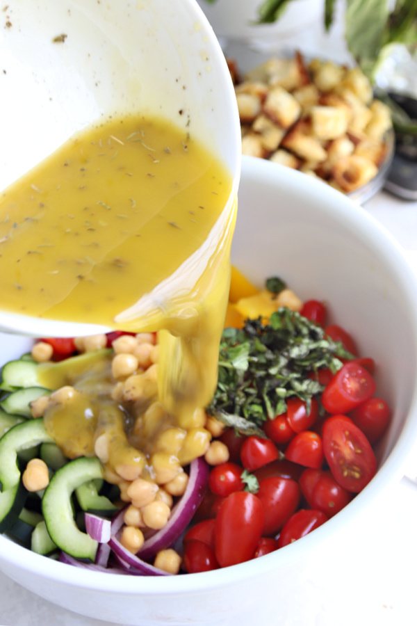 Tossing the dressing with fresh vegetables for Greek panzanella salad.