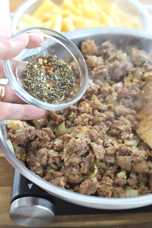 Adding tomato sauce to the browned Italian sausage for baked ziti casserole.