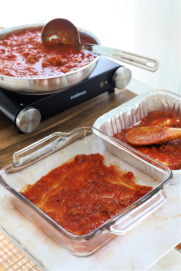 Beginning to layer the sauce, browned Italian sausage, mozzarella, ricotta, Parmesan and pasta for baked ziti casserole.